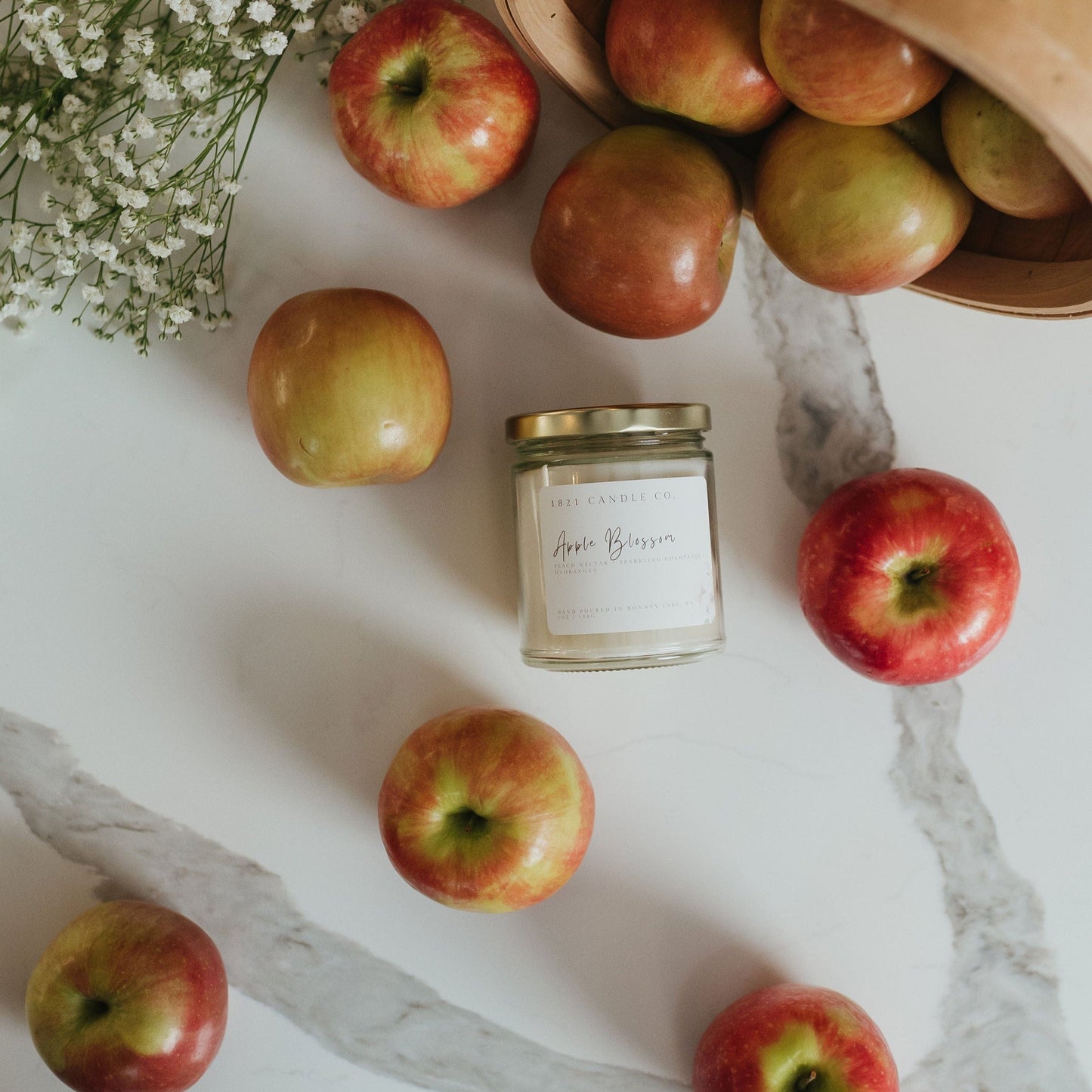 Overhead shot of Apple Blossom candle surrounded by scattered red apples on a farmhouse kitchen countertop