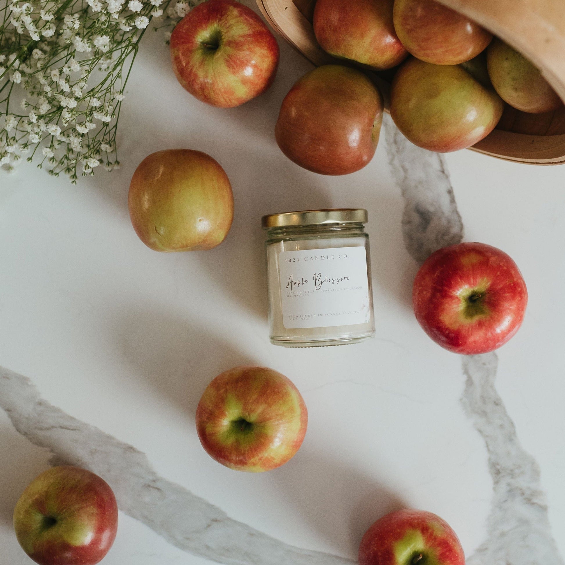 Overhead shot of Apple Blossom candle surrounded by scattered red apples on a farmhouse kitchen countertop