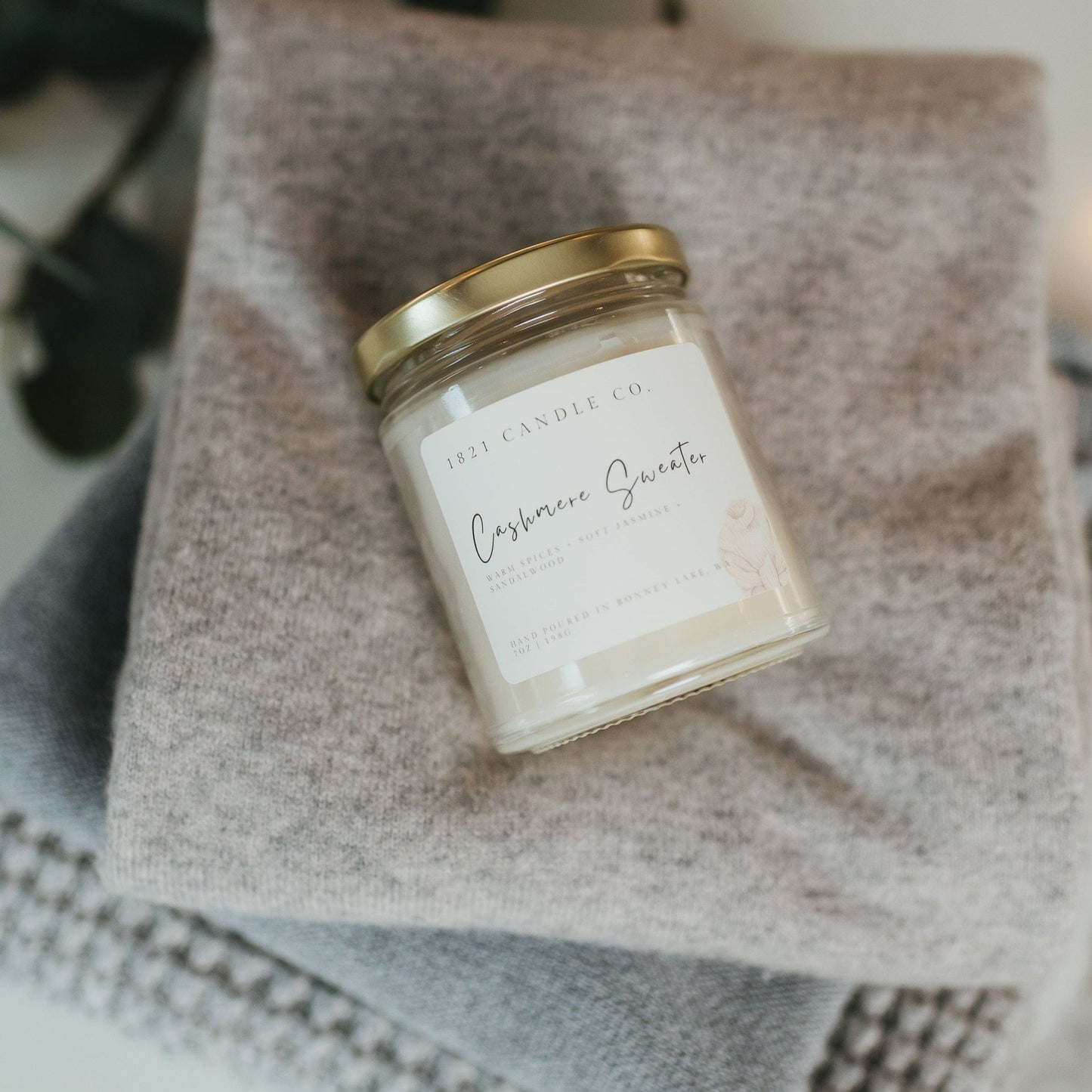 Cashmere Sweater candle by 1821 Candle Co. styled on a cozy folded sweater stack, perfect for home decor and relaxing moments.