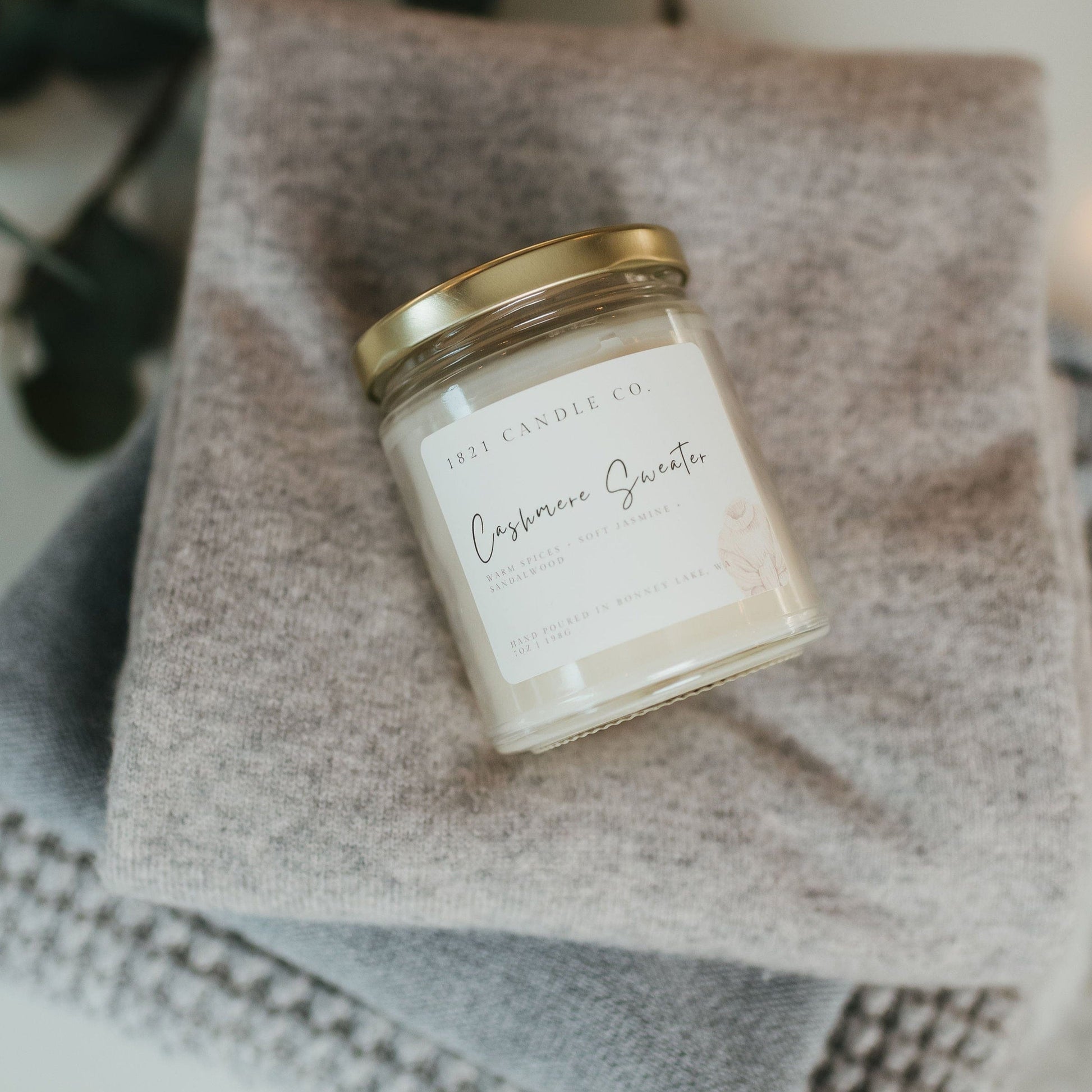 Cashmere Sweater candle by 1821 Candle Co. styled on a cozy folded sweater stack, perfect for home decor and relaxing moments.