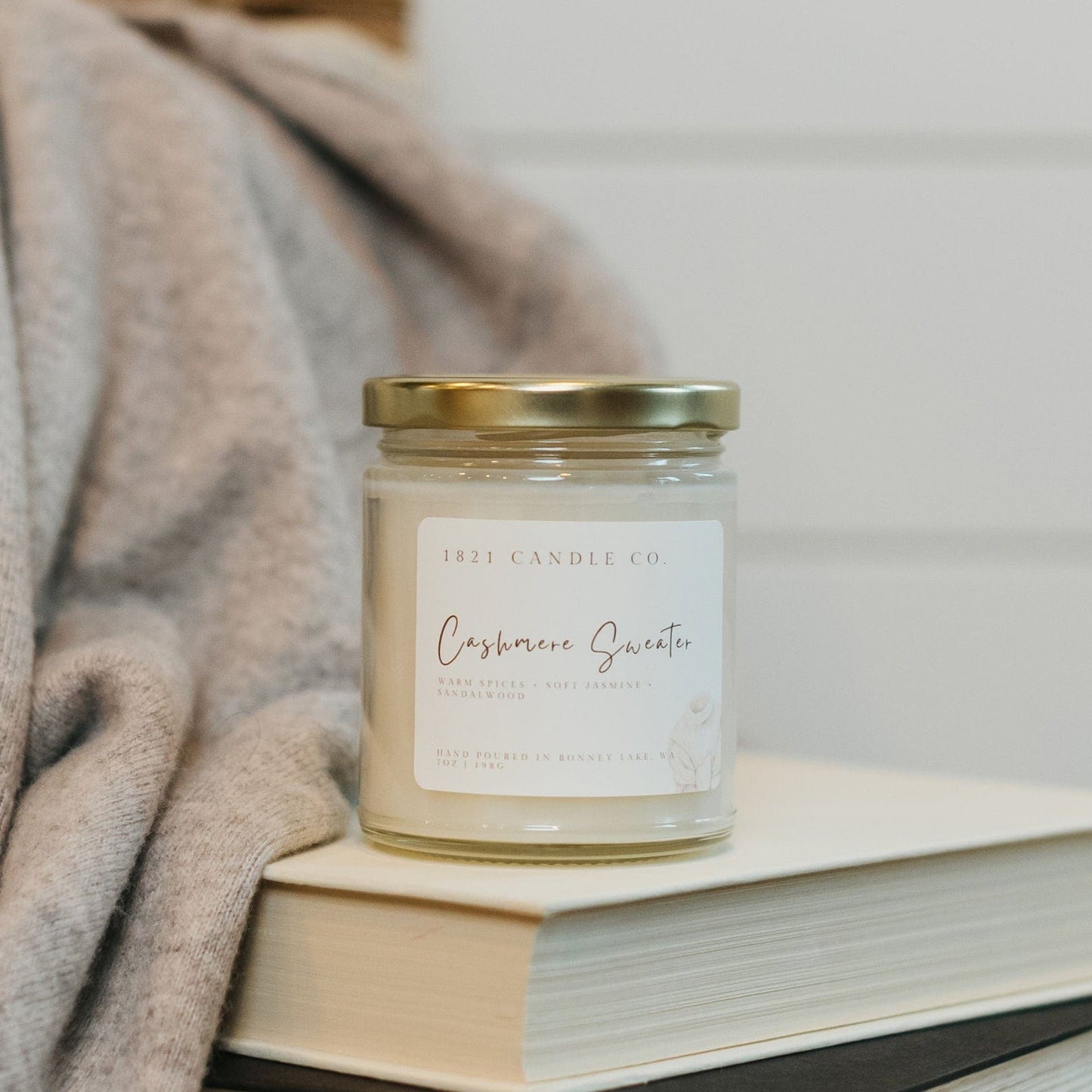 Cashmere Sweater candle by 1821 Candle Co styled on a stack of books with a soft knit sweater - perfect year round candle for book lovers and cozy hoe aesthetics.