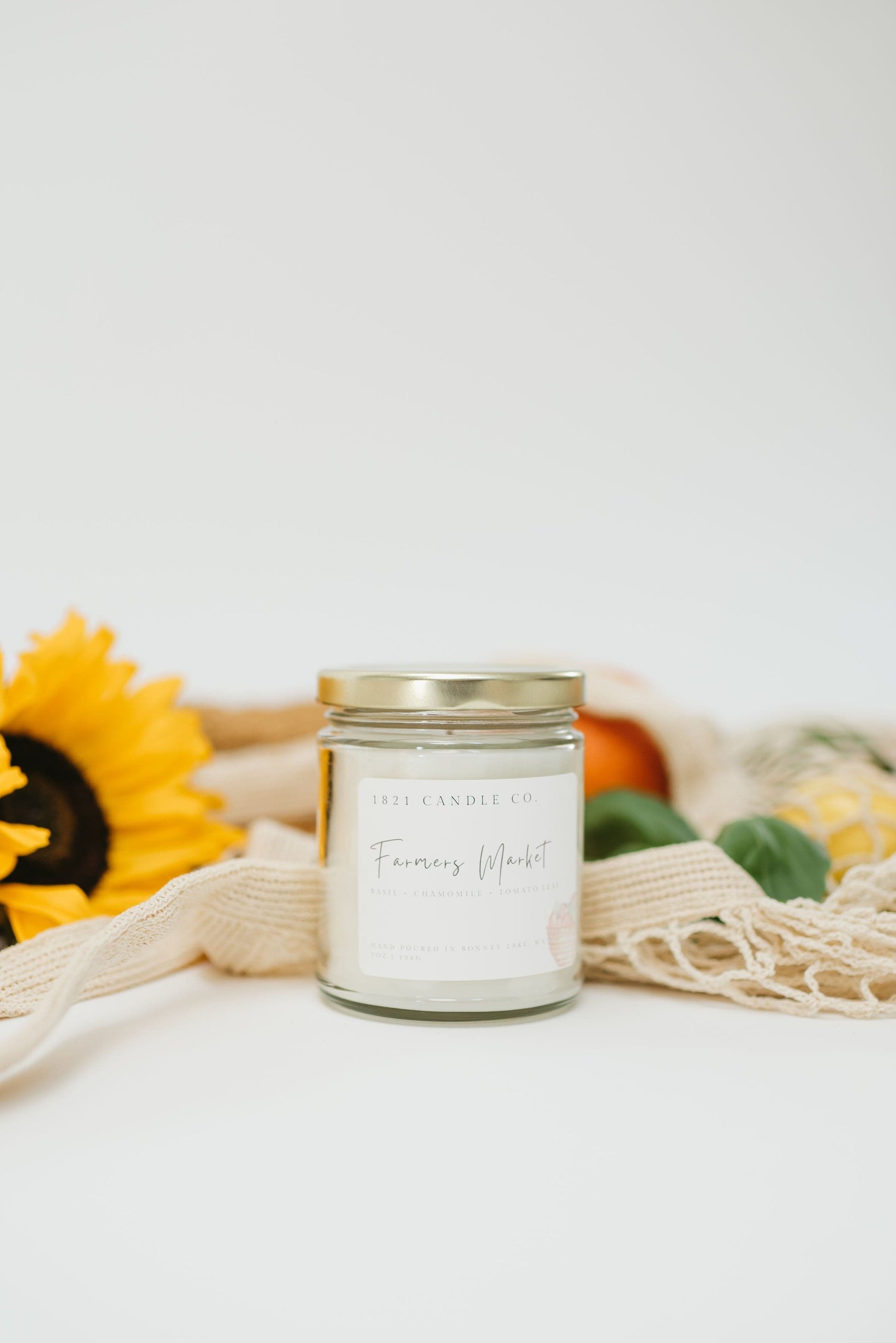 1821 Candle Co Farmers Market scented handmade candle displayed in a market style basket, featuring fresh citrus, basil and sunflowers.