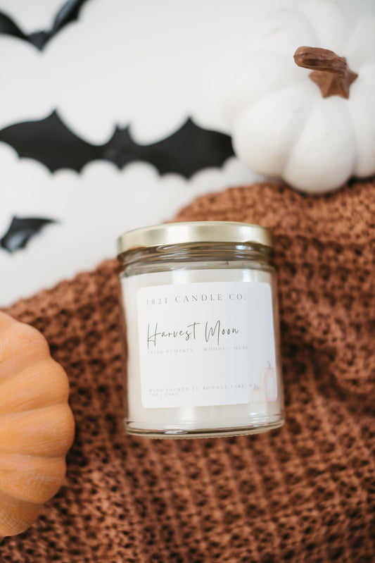 Clear candle jar with gold lid called Harvest Moon featuring notes of pumpkin, patchouli, spiced apple, leaves. Halloween scented farmhouse candle.