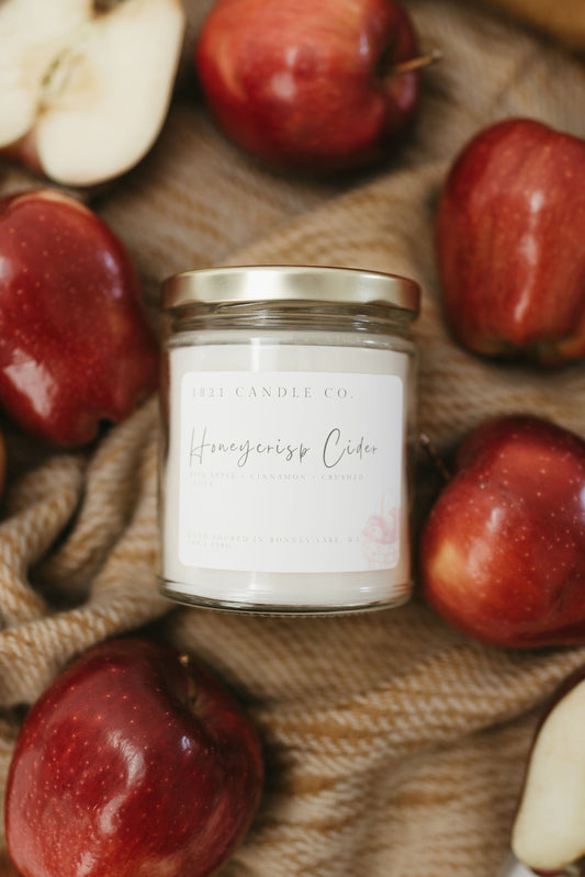 Honeycrisp Cider soy blend candle surrounded by red apples on a woven  fall colored fabric