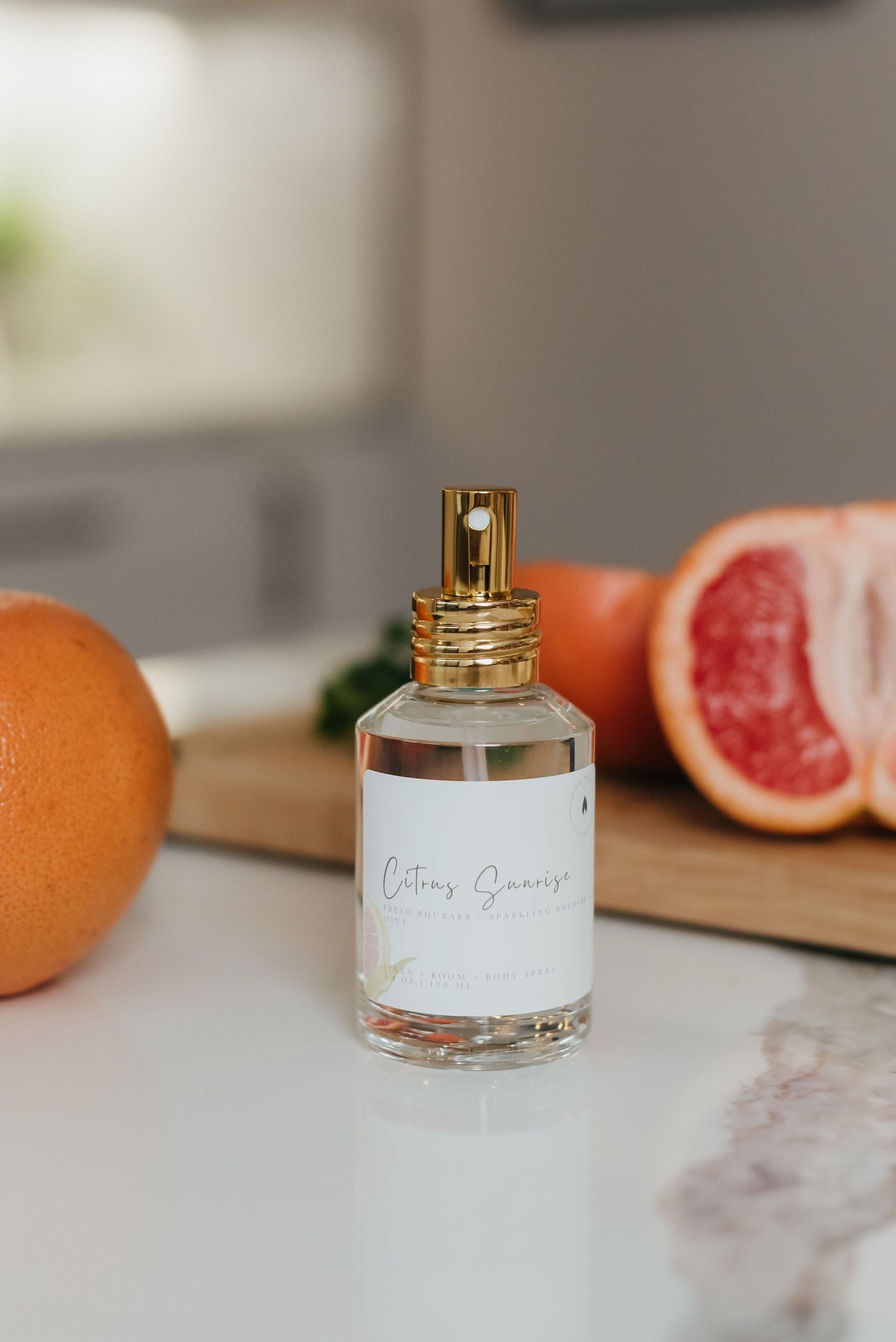 Natural room spray labeled Citrus Sunrise, featuring notes of rhubarb, grapefruit and mint, styled in a cozy kitchen scene with citrus - perfect for refreshing any room naturally.