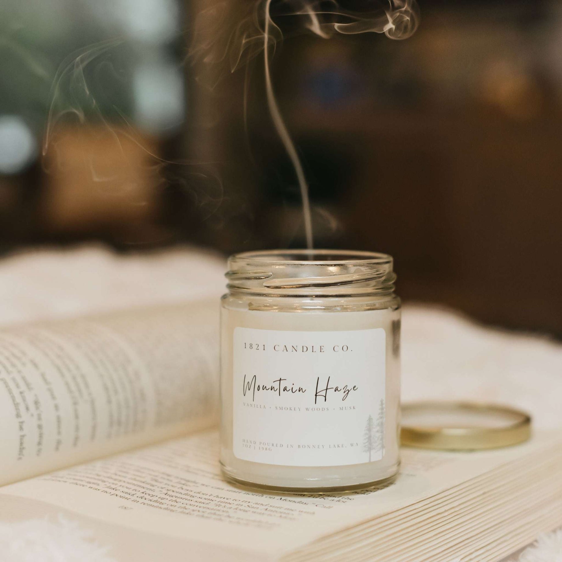 Handmade candle made in Bonney Lake, Wa by 1821 Candle Co. Mountain Haze candle sitting on an open book with a modern farmhouse style aesthetic. Notes of lavender, musk, woods, vanilla.