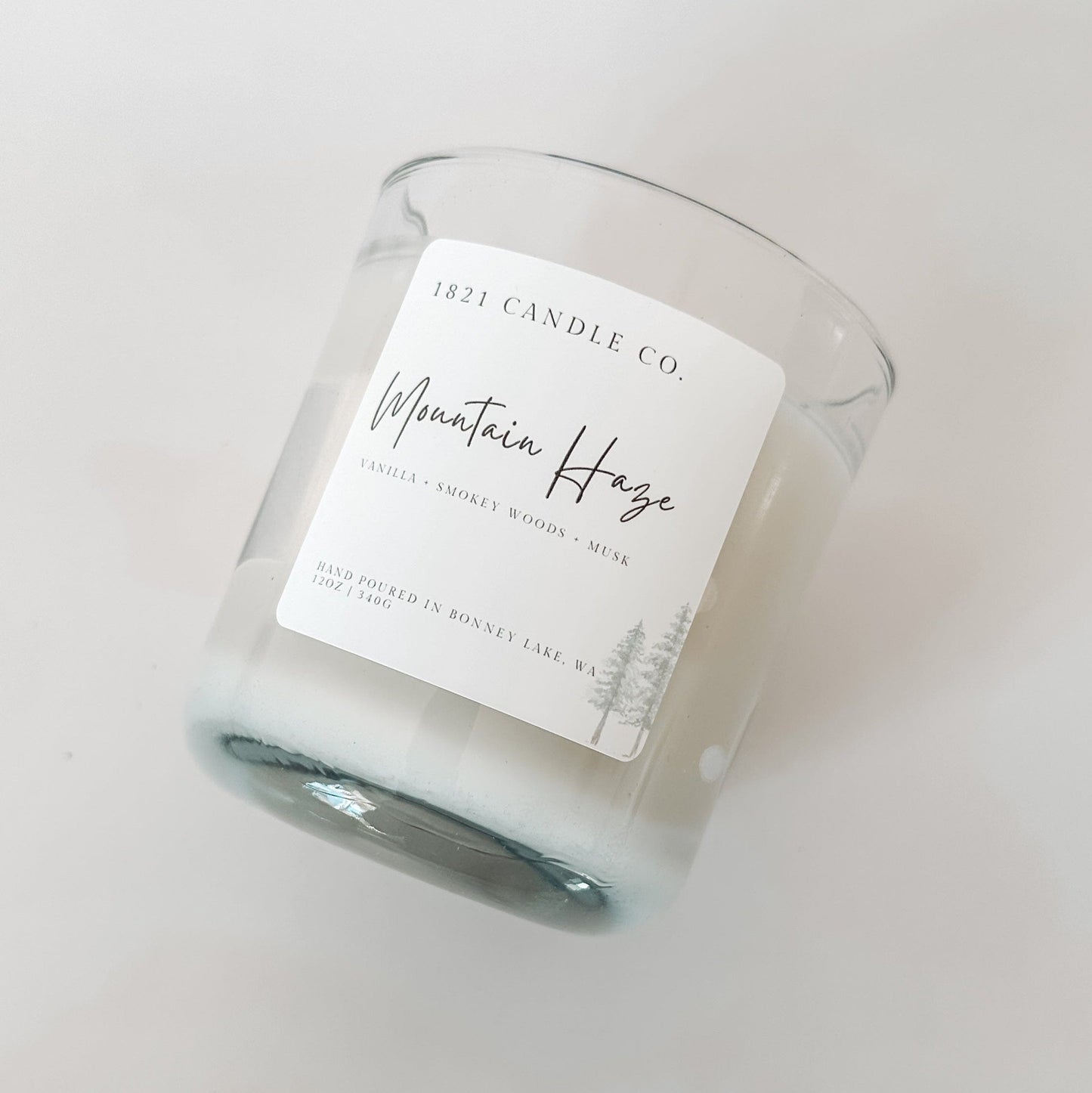 Clear glass candle labeled Mountain Haze by 1821 Candle Co. featuring a minimalist design with warm vanilla, smokey woods and musk notes.