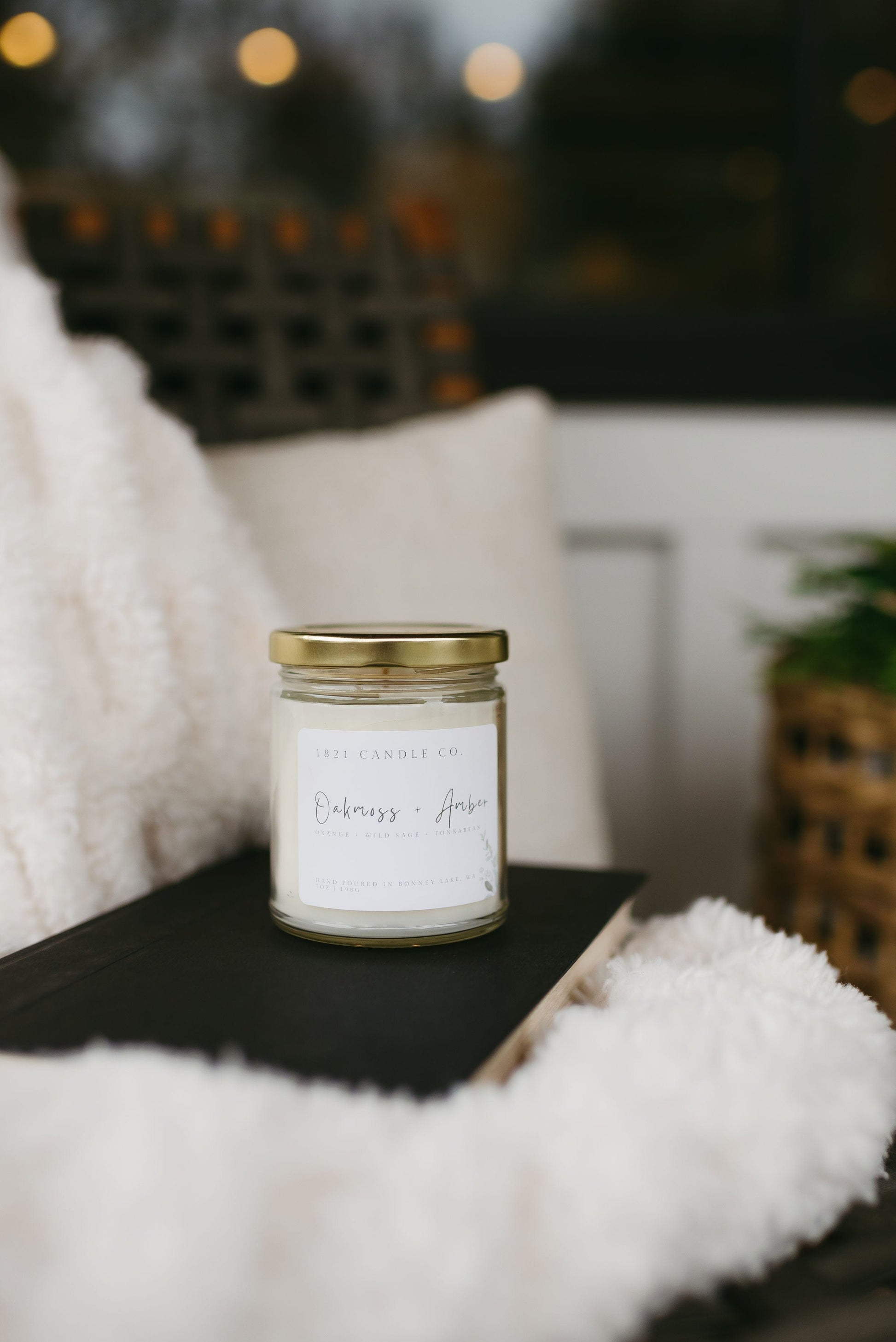 Oakmoss Amber candle on a cozy porch chair with a soft white blanket and book - perfect for slow living and cozy home decor.