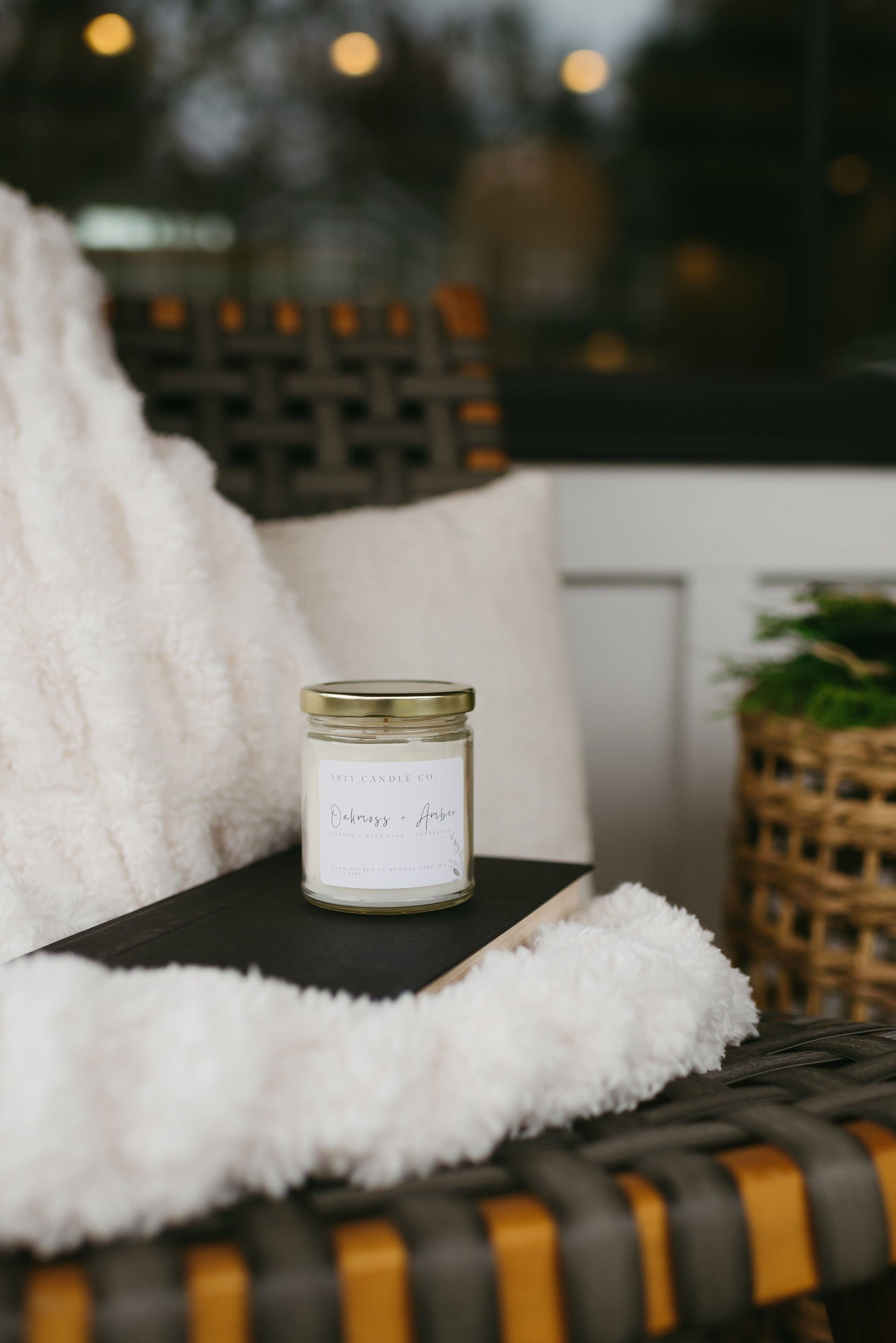 Oakmoss Amber jar candle styled on a cozy outdoor patio chair - warm amber candle for relaxing slow mornings.