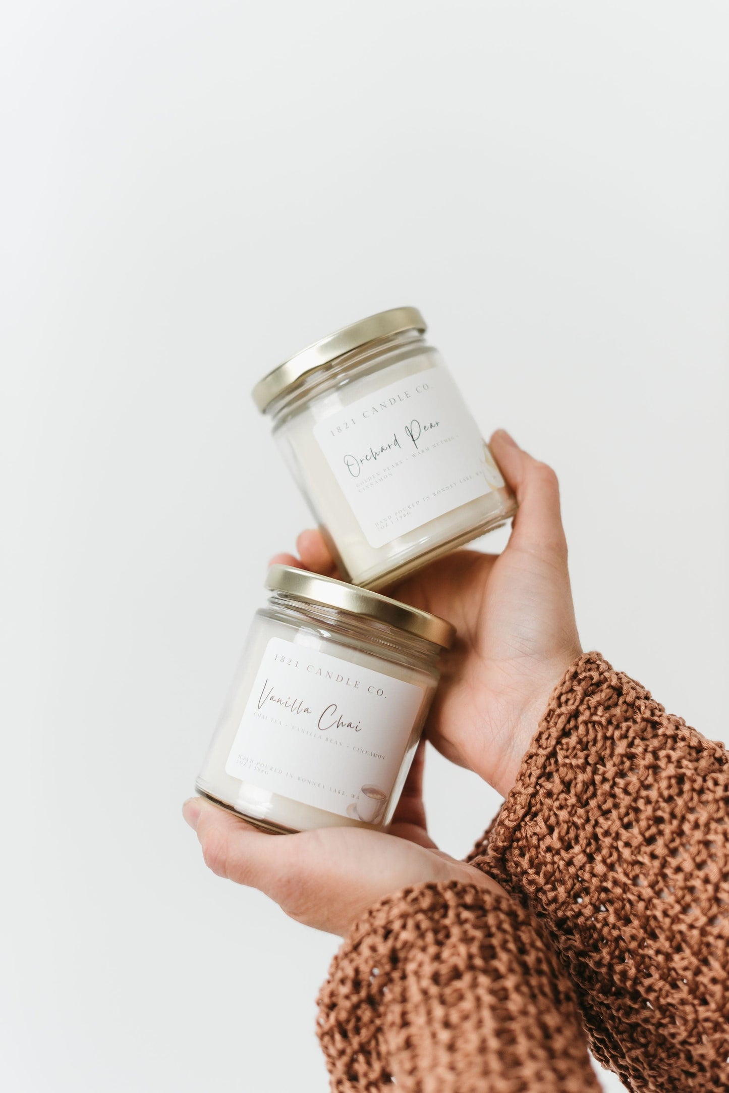 Orchard Pear and Vanilla Chai Fall Candles held in someone's hands against a white background.