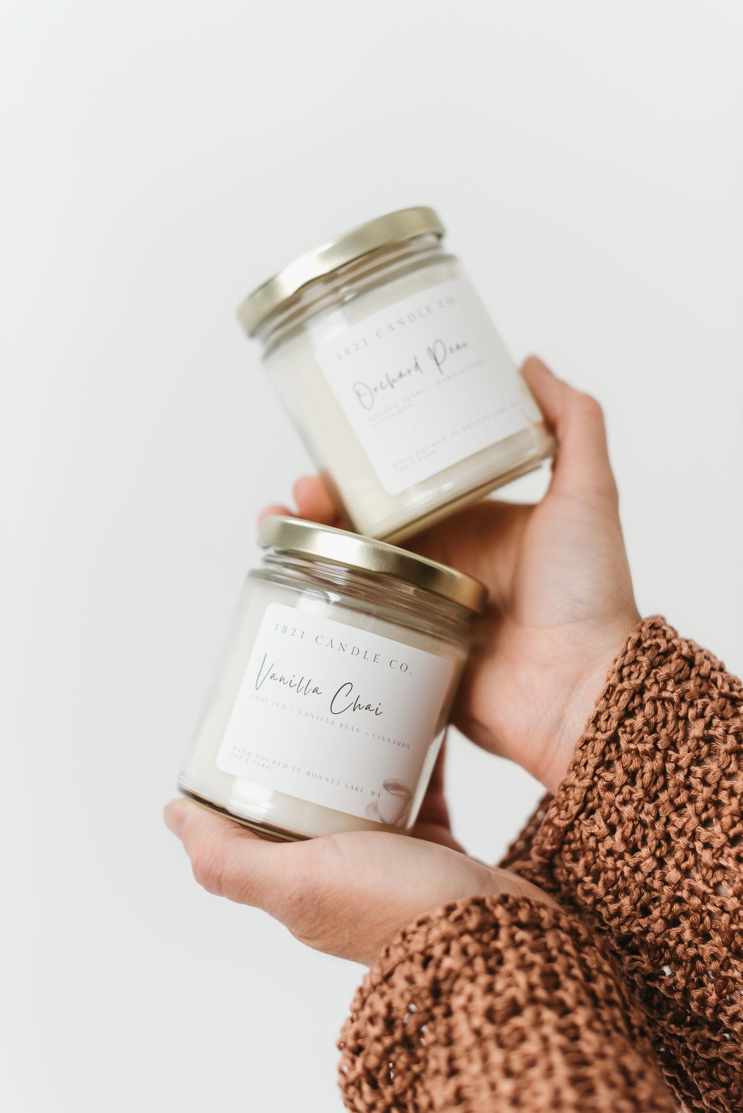 Vanilla Chai and Orchard Pear fall scented candles held in a hand with a white background