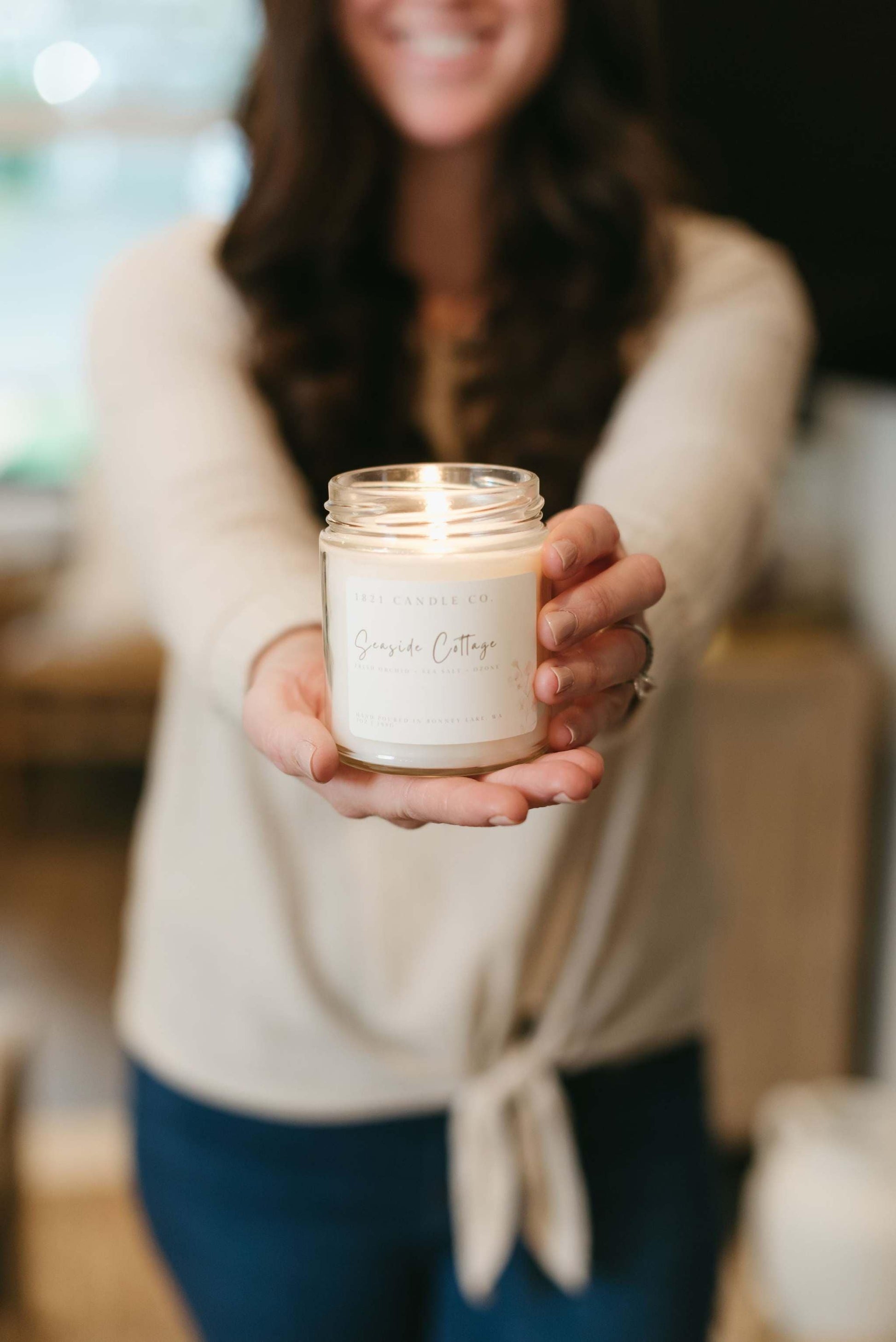 Seaside Cottage, a beautifully crafted handmade candle with a minimalist label, placed in a warm, rustic living room setting with natural textures and soft lighting.