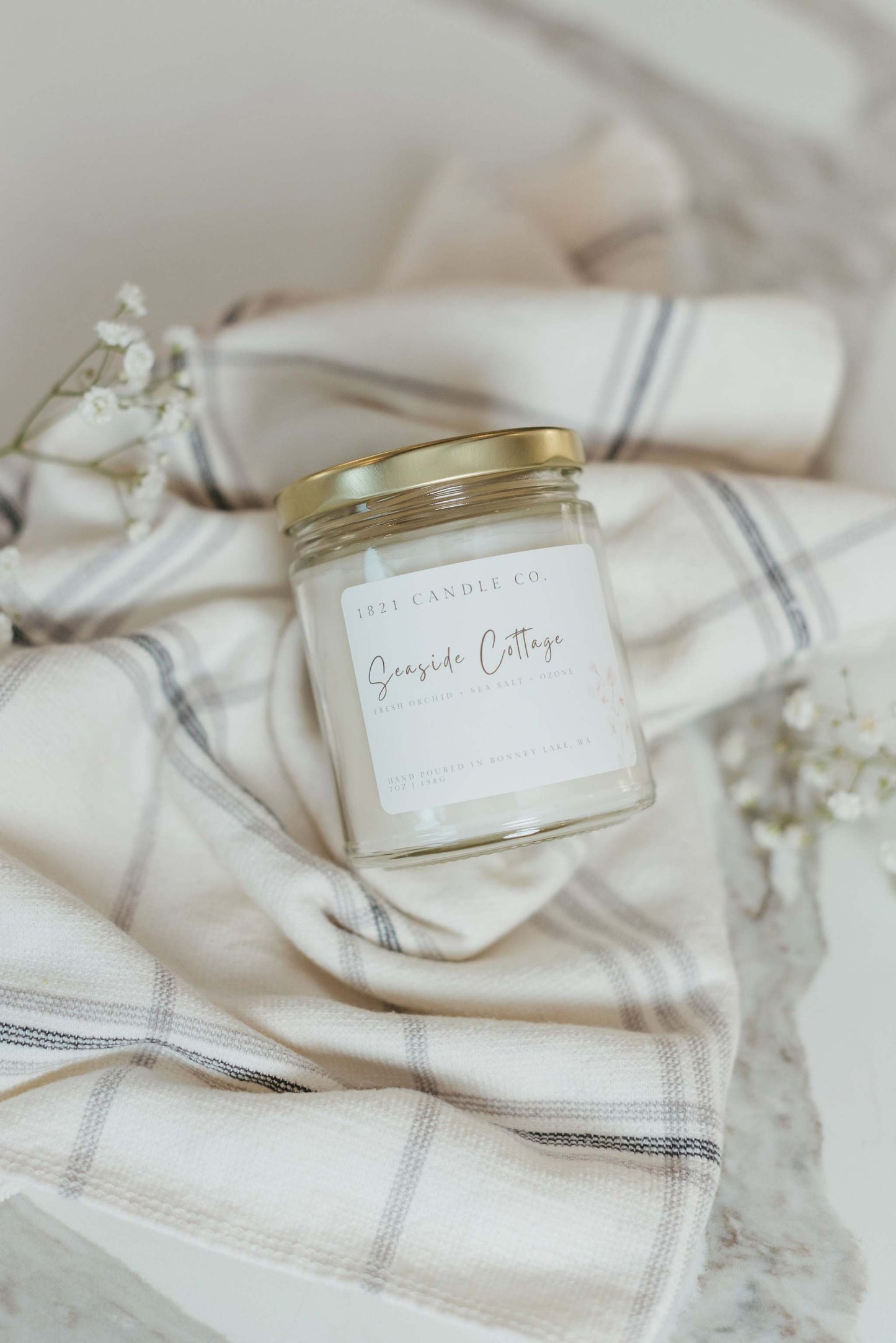 Neutral toned soy blend candle called Seaside Cottage in a clear glass jar, resting on a soft linen backdrop. Aesthetic and calming beach home decor for a fresh and inviting ambiance.