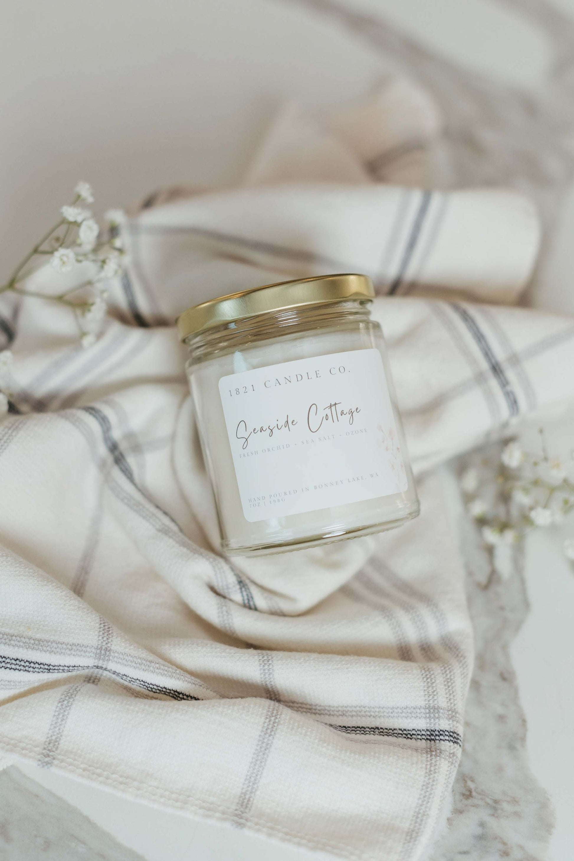 Neutral toned soy blend candle called Seaside Cottage in a clear glass jar, resting on a soft linen backdrop. Aesthetic and calming beach home decor for a fresh and inviting ambiance.