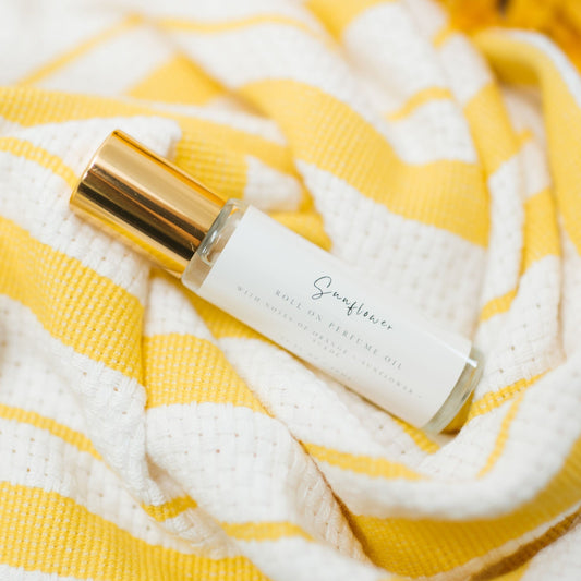 Sunflower Roller Ball Perfume made with Coconut Oil and skin safe fragrance oil. A classic gold capped bottle with a minimalist farmhouse style label laying on a bright stripped yellow kitchen towel.