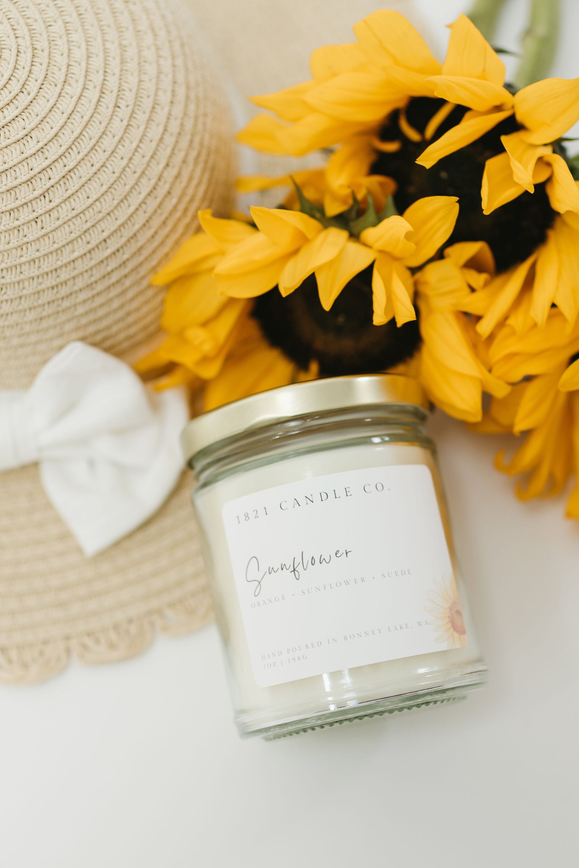 Sunflower scented soy blend candle by 1821 candle co resting against a straw hat and bright yellow flowers - perfect for summer slow living and thoughtful gift ideas
