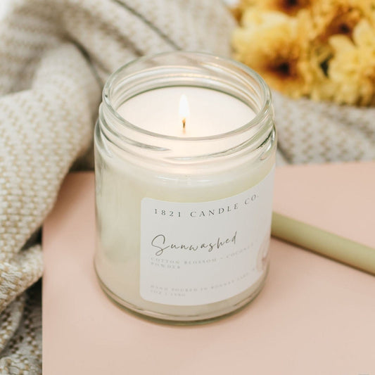 Hand poured clean burning Sunwashed candle with cotton blossom and coconunt scent, styled with cozy textures and fresh florals for a calming home vibe.
