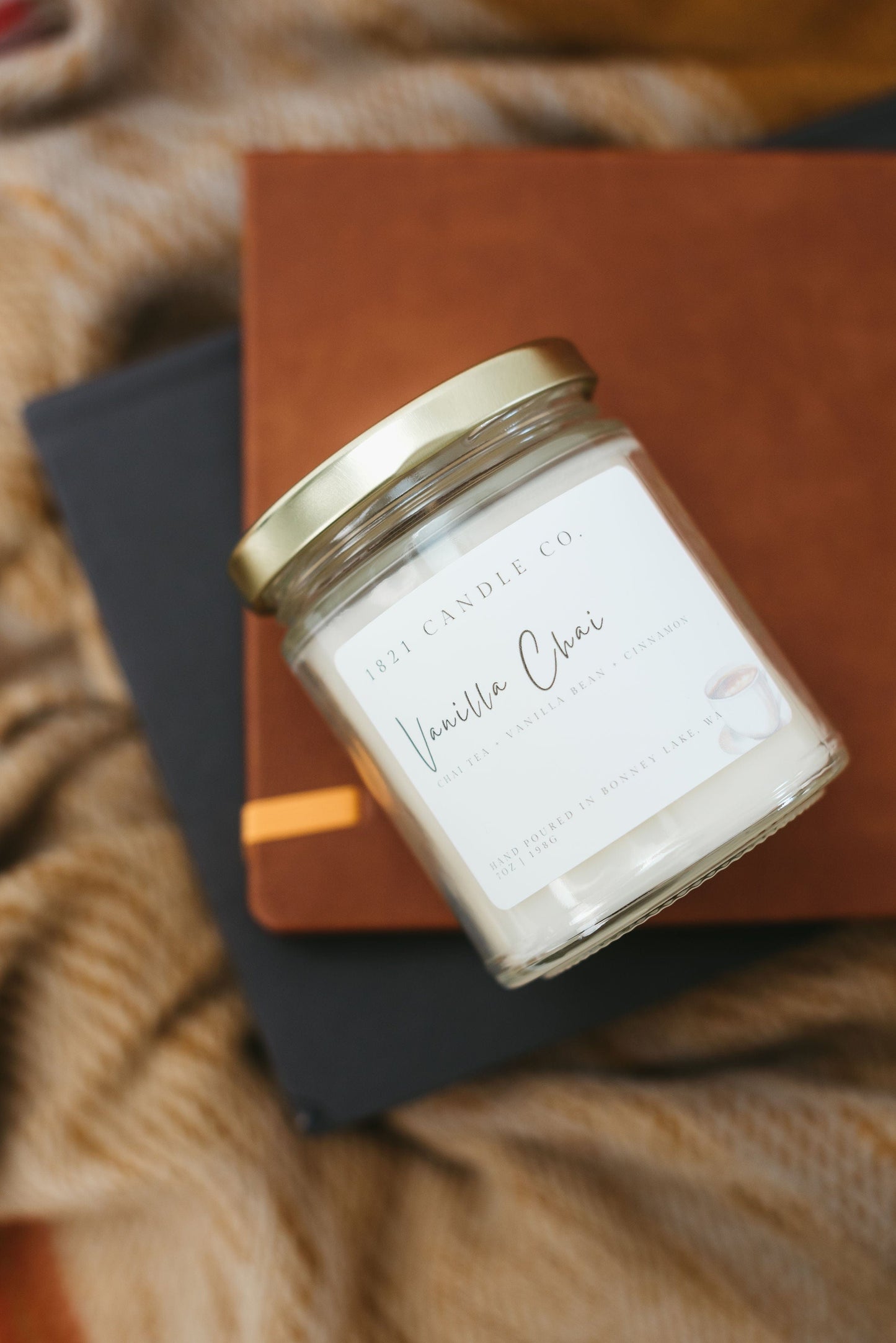 Vanilla Chai Candle in a clear vessel with gold lid laying on it's side with a stack of books underneath.