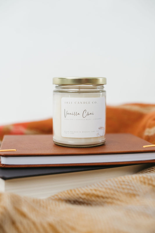 Vanilla Chai coffee inspired candle sitting on a stack of books with a warm cozy blanket underneath and in the background.