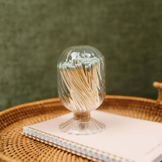 Glass match cloche filled with sage green tipped safety matches, displayed on a wovem tray - an elegant and functional candle accessory by 1821 Candle Co.