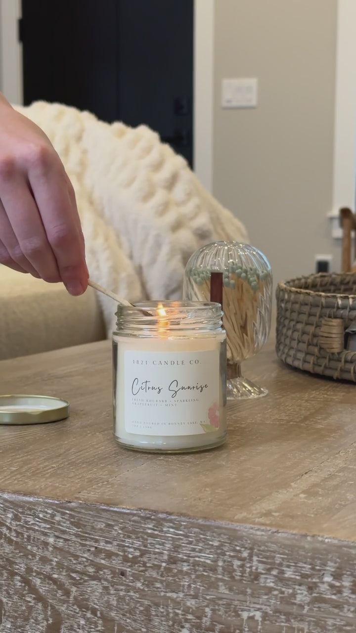 Citrus Sunrise Candle by 1821 Candle Co being lit with a glass match cloche