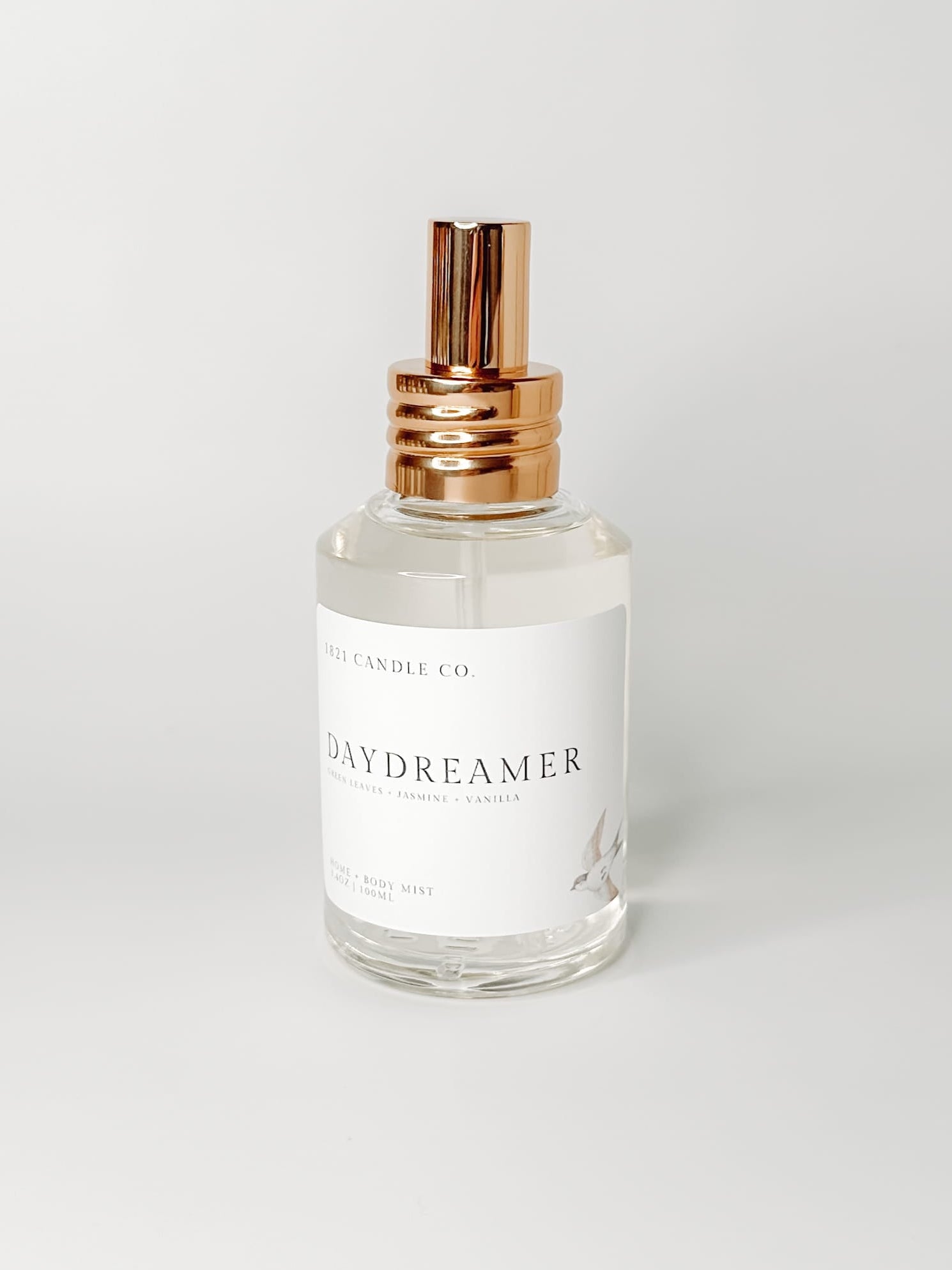 Daydreamer Home and Body Mist with notes of sandalwood, creamy vanilla and soft jasmine in a clear glass bottle and gold spray cap on a white background.