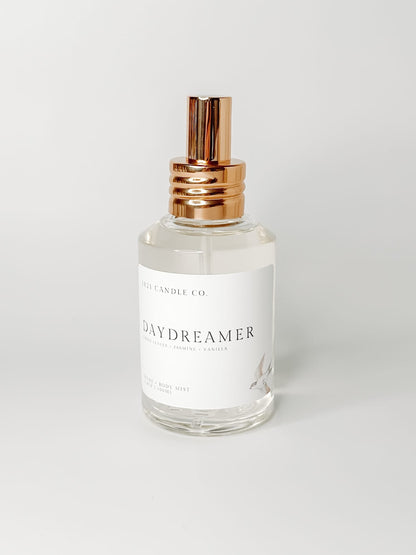 Daydreamer Home and Body Mist with notes of sandalwood, creamy vanilla and soft jasmine in a clear glass bottle and gold spray cap on a white background.