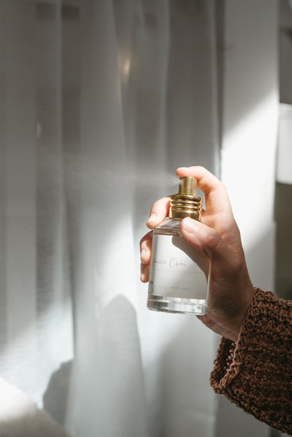 Hand spraying fall air freshener called Vanilla Chai against a white sheet curtain.