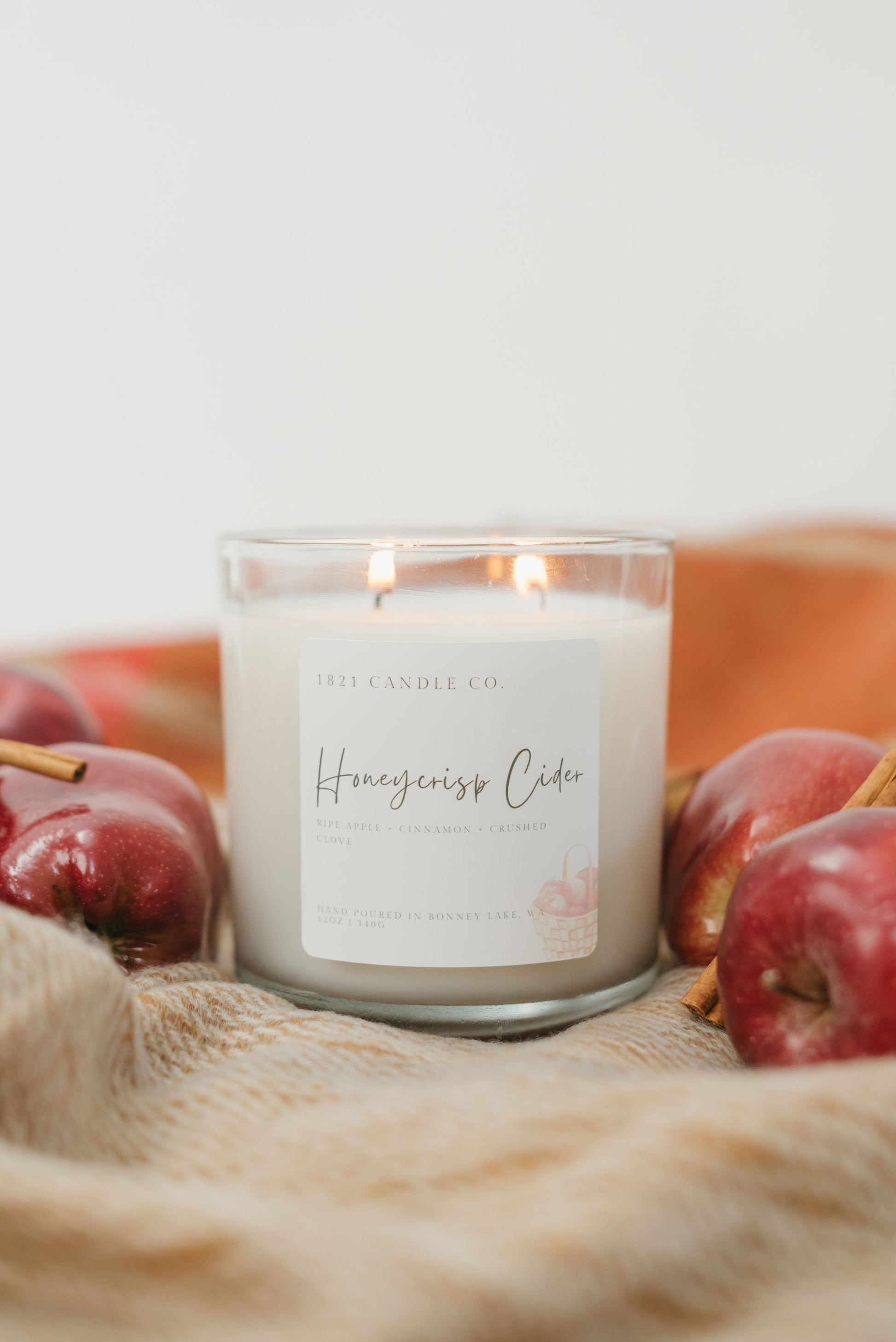 Soy Blend Candle called Honeycrisp Cider on a fall colored blanket surrounded by apples and cinnamon.
