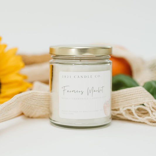Farmers Market candle by 1821 Candle Co next to a produce bag filled with fresh summer finds, perfect for summer home decor and cozy vibes.