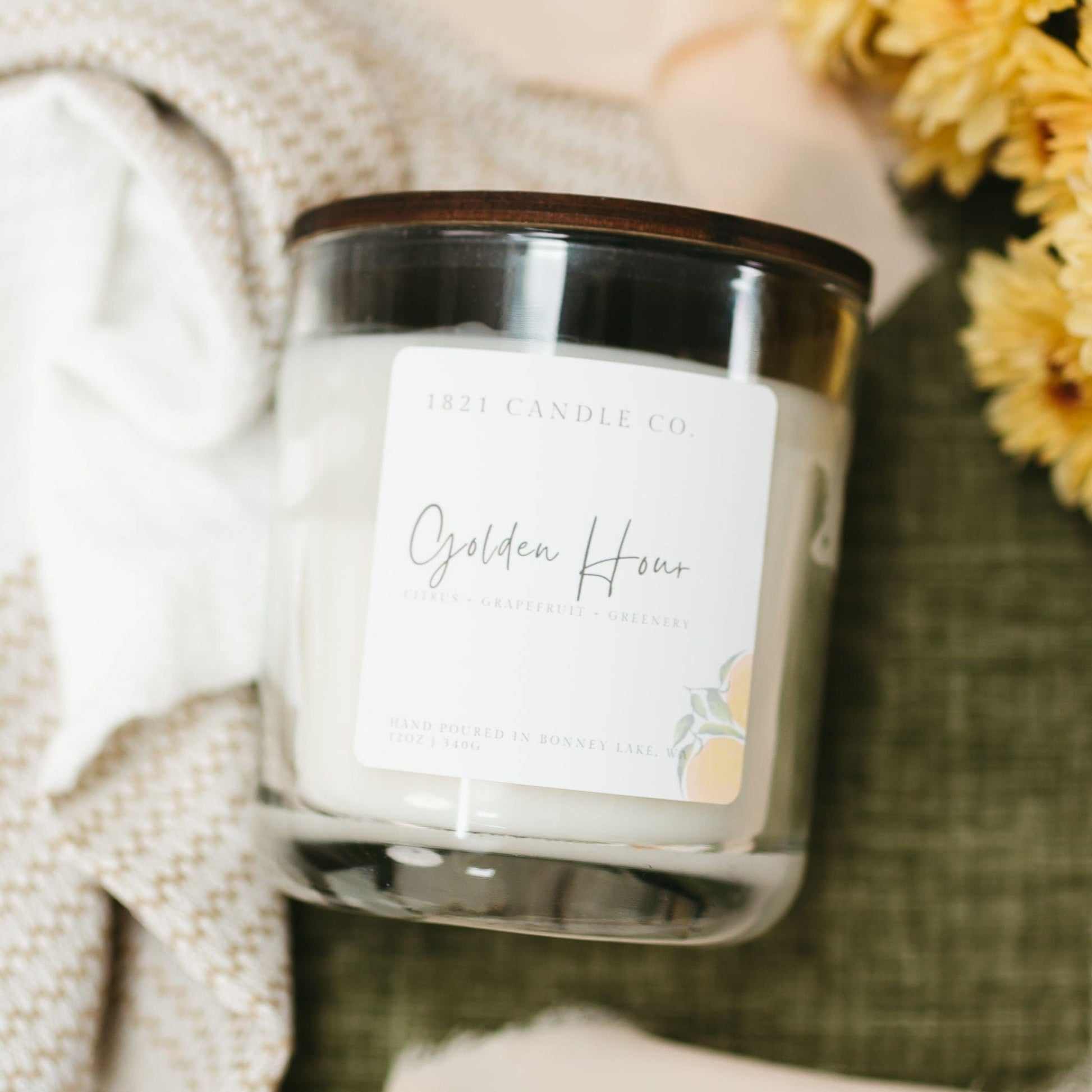Golden Hour Double Wicked 12oz Soy Blend Candle by 1821 Candle Co with citrus and greenery notes, styled with yellow flowers and cozy textures for a summer home fragrance aesthetic.