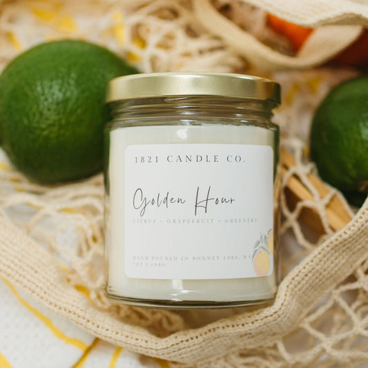 Golden Hour 7oz citrus candle by 1821 Candle Co. nestled in a mesh market bag with fresh limes and oranges, perfect for cozy summer mornings and farmhouse kitchen decor.