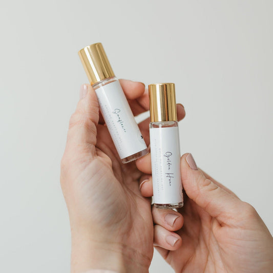 Hands holding Golden Hour and Sunflower roll on perfumes with gold caps. Handmade coconut oil based fragrance from 1821 Candle Co.
