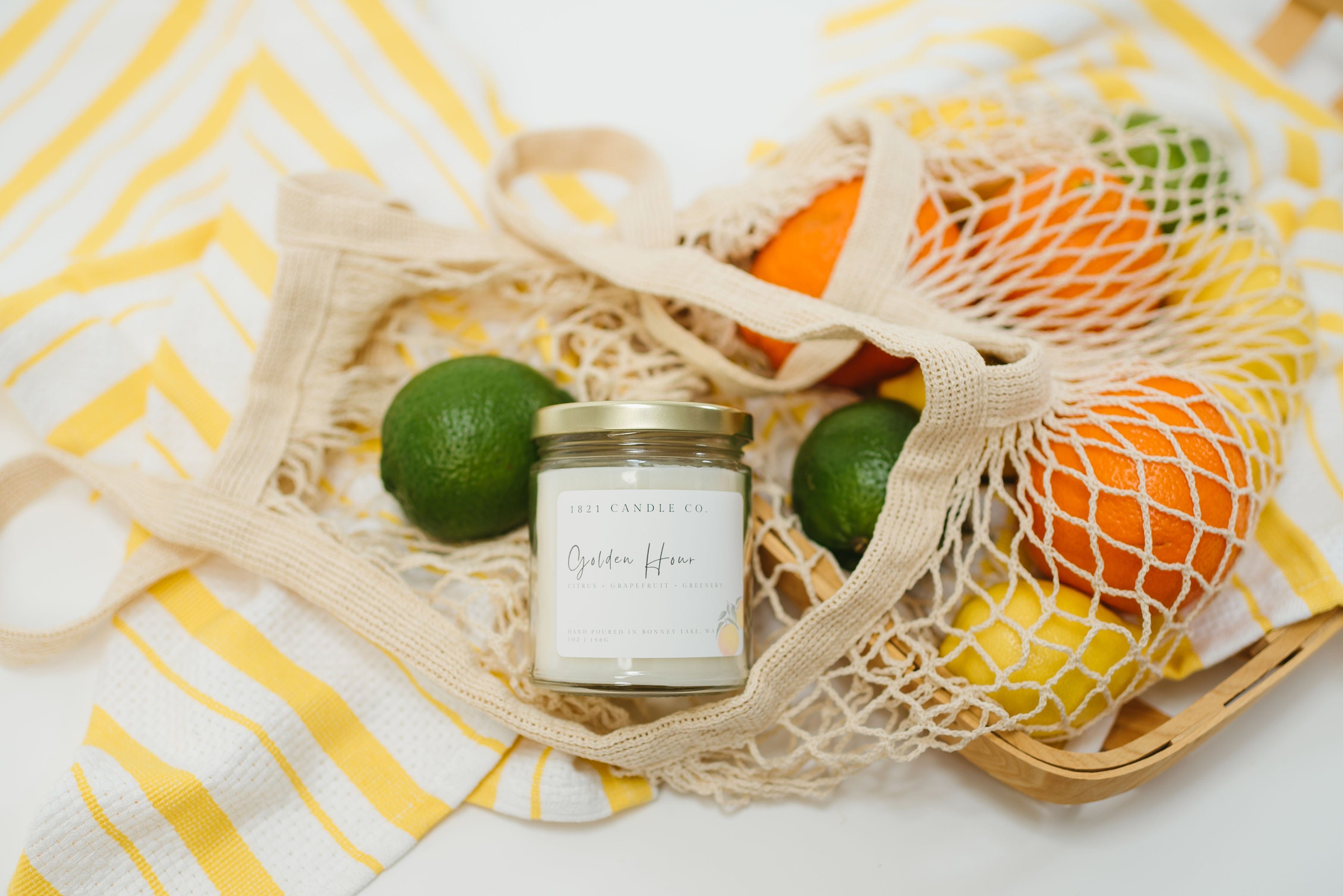 Flay lay of Golden Hour grapefruit and greenery scented candle in a market tote with oranges and limes, eco friendly 7oz candle for  summer gifting or natural home fragrance.