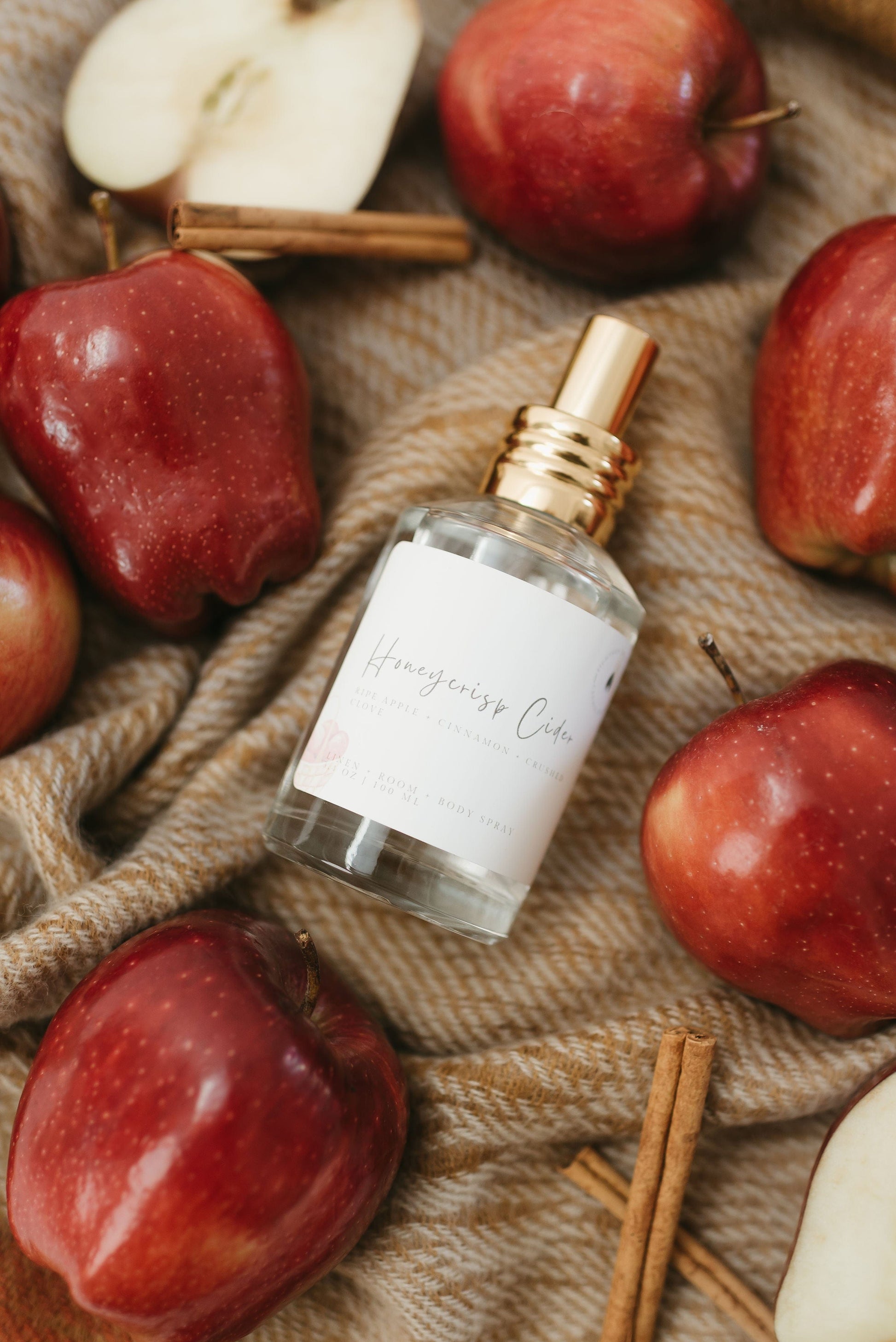 Honeycrisp Cider Linen Spray, Room Spray, Body Spray surrounded by red apples and cinnamon sticks on a fall inspired blanket