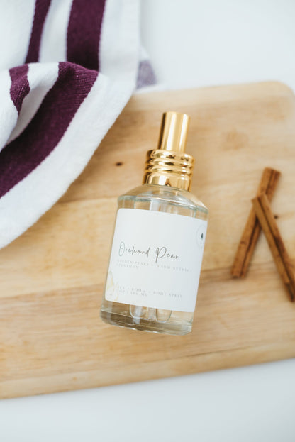 Bottle of Orchard Pear linen, room, body spray  on a wooden surface with cinnamon sticks and a towel in the background.
