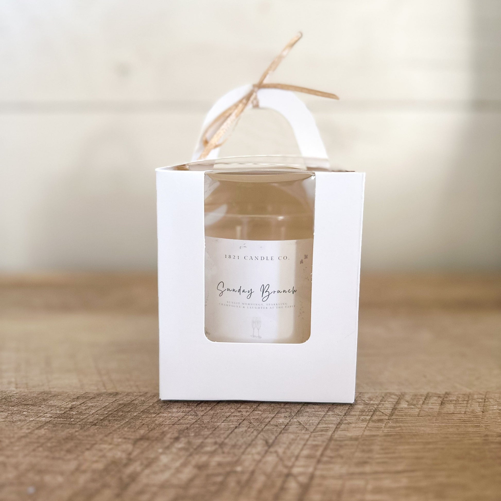 Sunday Brunch Limited Edition Coconut Apricot Wax Candle in a white gift box with window and handle and a champagne colored box on top.