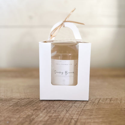 Sunday Brunch Limited Edition Coconut Apricot Wax Candle in a white gift box with window and handle and a champagne colored box on top.