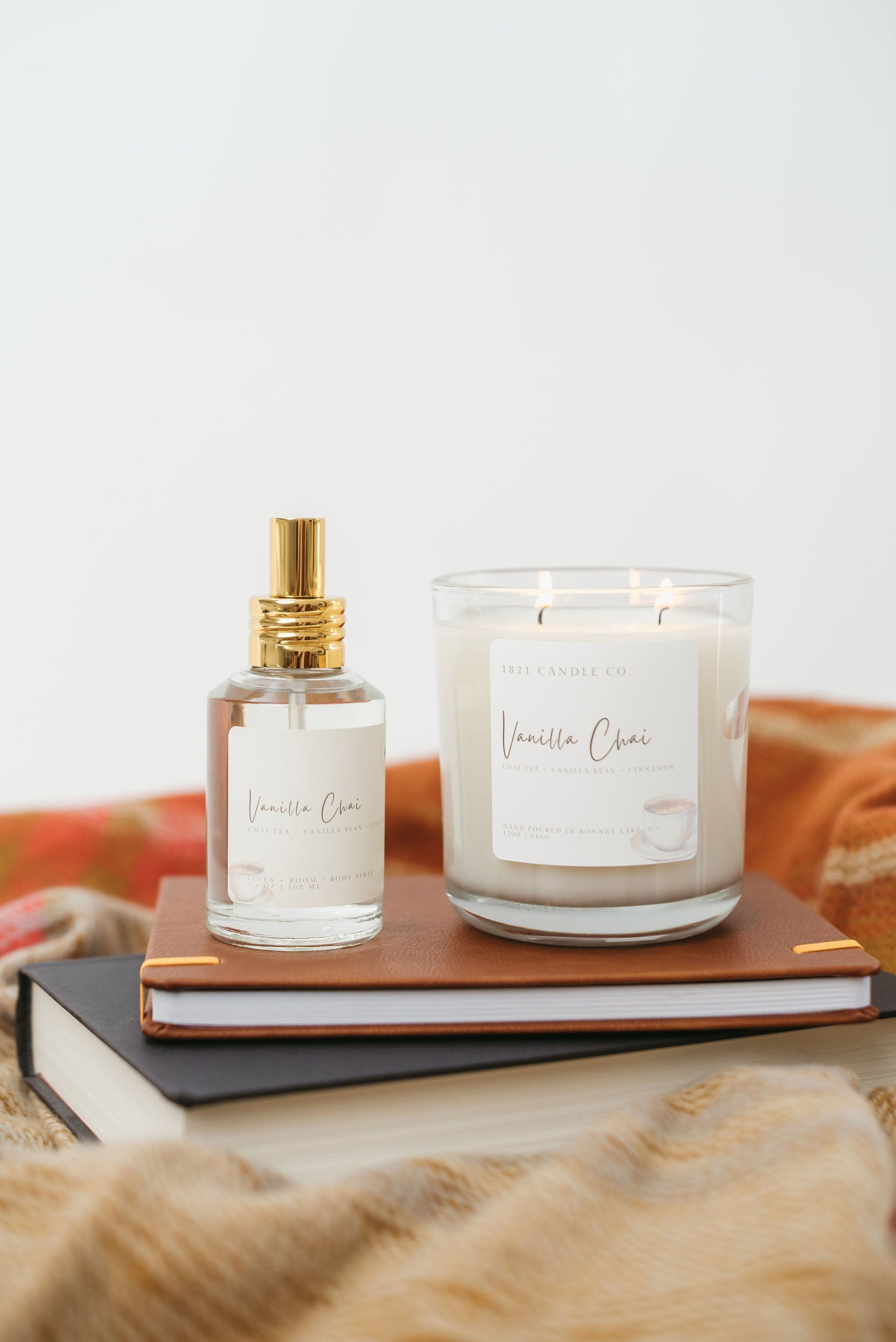 Vanilla Chai Candle and Room Spray sitting on top of a stack of books under a warm toned sweater