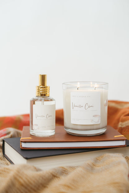Vanilla Chai Candle and Room Spray sitting on top of a stack of books under a warm toned sweater