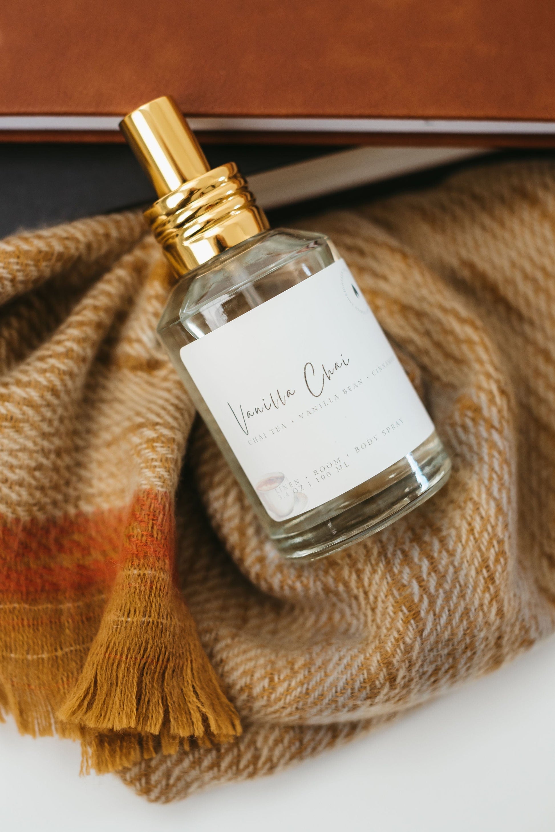 Vanilla Chai Fall Scented Home Air Freshener laying on it's side with warm colored blanket and books underneath.