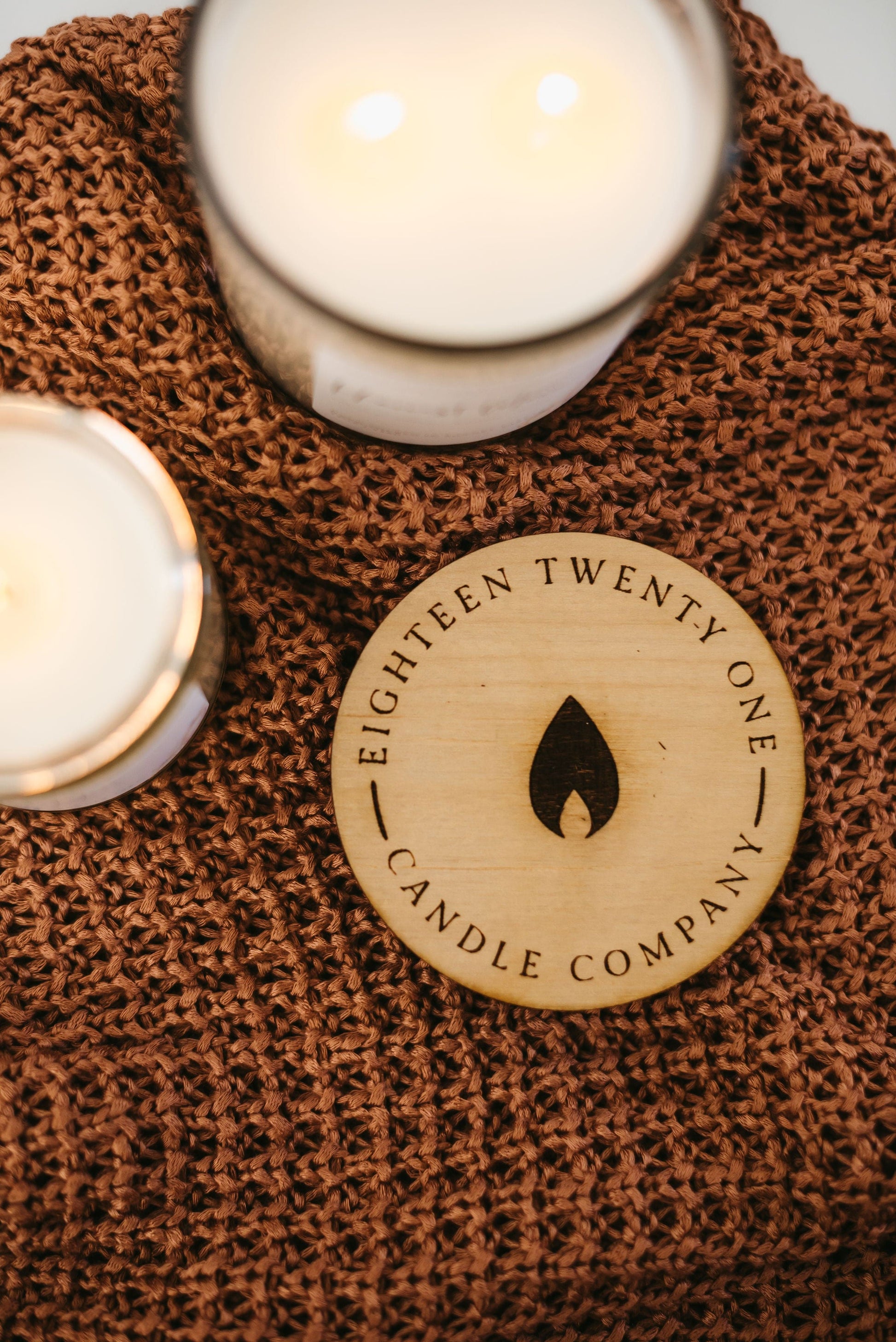 Two candles on a textured surface with 'Eighteen Twenty One Candle Company' branded wooden lid.