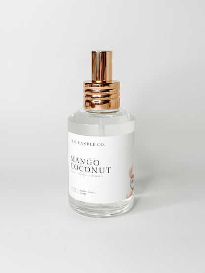 Mango Coconut room, linen, body spray with notes of peach, mango, coconut on a clear glass spray bottle with a gold cap made by 1821 candle co in washington. Displayed on a white background.