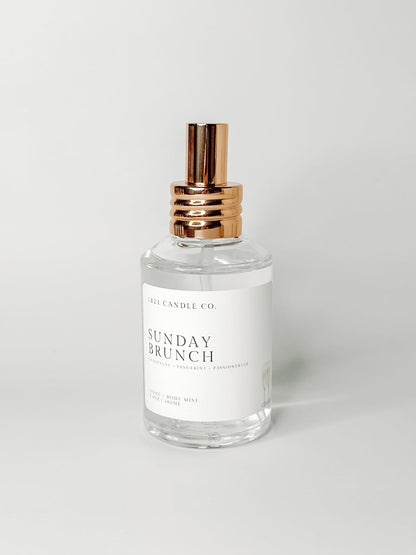 sunday brunch home air freshener and body mist by 1821 candle co in a clear glass bottle with gold spray cap on a white background.